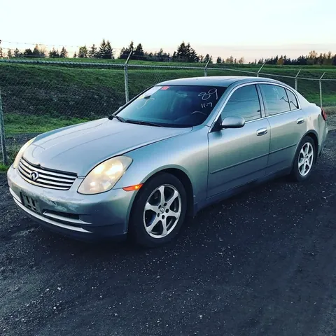 Silver Infiniti sedan in a salvage yard, lot markings written on the windscreen